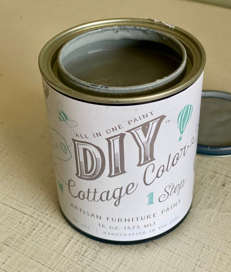 Open can of DIY Paint Co. Gray Skies Cottage Color with lid on beige surface.
