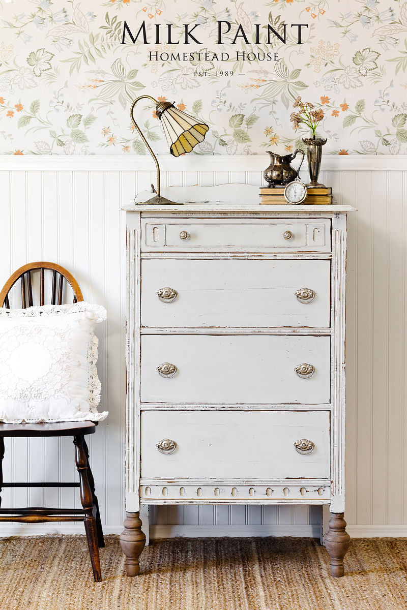 Vintage white dresser painted with Homestead House Grey Silk Milk Paint next to a wooden chair.