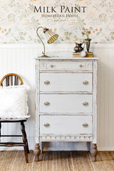 Vintage white dresser painted with Homestead House Grey Silk Milk Paint next to a wooden chair.
