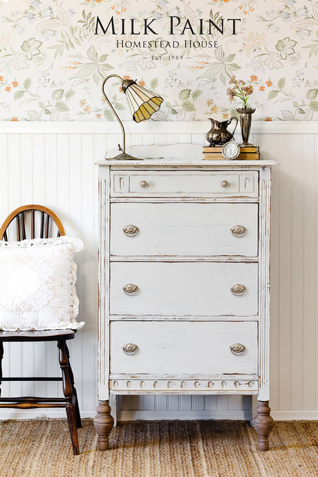 Vintage white dresser painted with Homestead House Grey Silk Milk Paint next to a wooden chair.