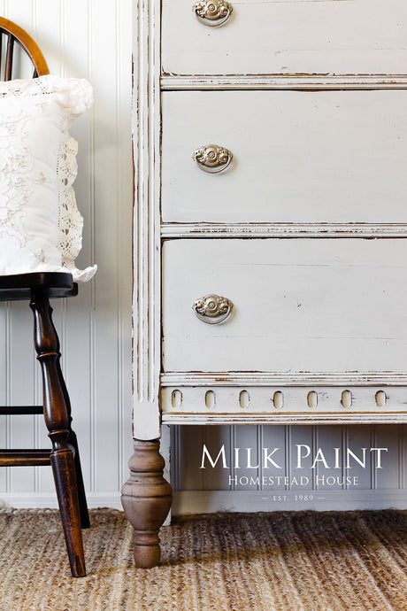 Dresser in Homestead House Grey Silk Milk Paint with ornate pulls, next to a wooden chair on a textured rug.