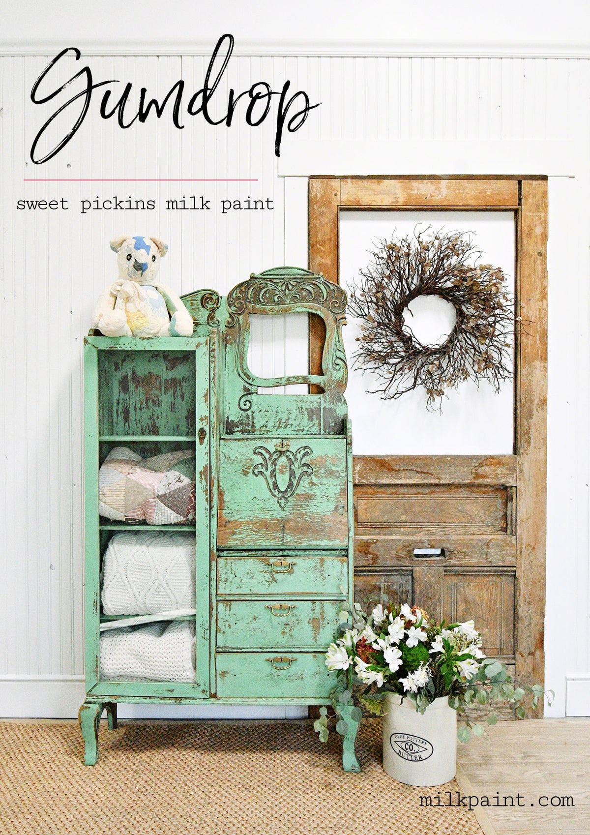 Cabinet painted in Gumdrop by Old Fashioned Milk Paint, storing linens and a teddy, near a door with a wreath.