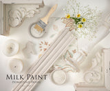Gustavian White Milk Paint by Homestead House with brush, candles, floral tiles, and yellow flowers arranged flat.
