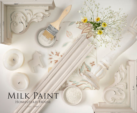 Gustavian White Milk Paint by Homestead House with brush, candles, floral tiles, and yellow flowers arranged flat.