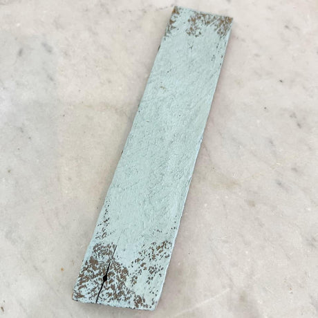 Narrow distressed slat painted in DIY Paint Co. Haint Blue Cottage Color on a white marble surface.