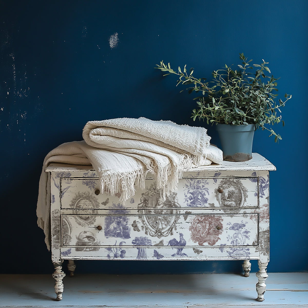 Hameau de la Reine Paint Inlay dresser by I.O.D. with cream blankets and a plant.