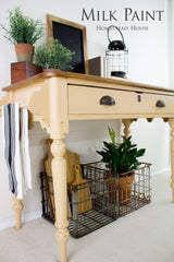 Table painted with Homestead House Hampton Milk Paint, displaying plants, decor, and cutting boards in a wire basket below.