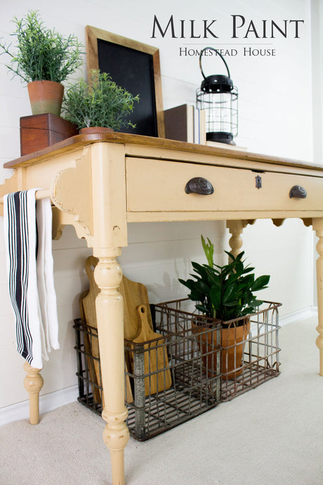 Table painted with Homestead House Hampton Milk Paint, displaying plants, decor, and cutting boards in a wire basket below.