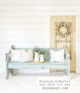 Harbor by Old Fashioned Milk Paint light blue bench with pillows, jug, and lavender near a cream door.