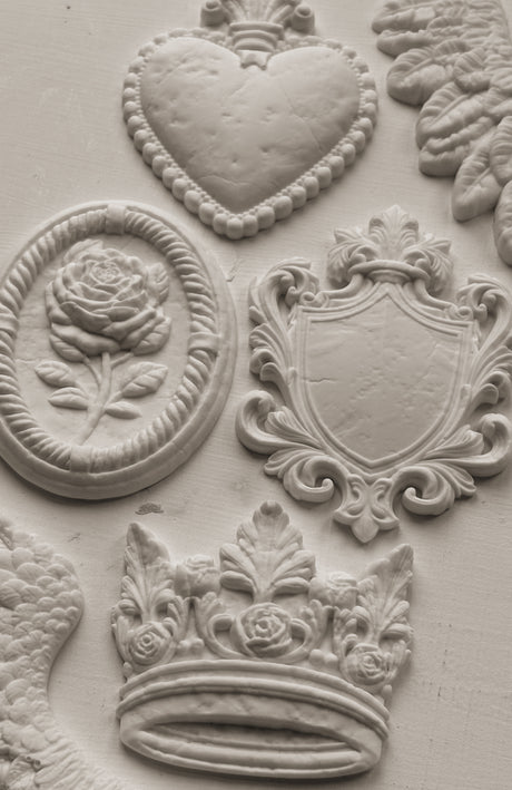 I.O.D. Heraldry Mould white reliefs with hearts, roses, shields, and crowns in decorative designs.