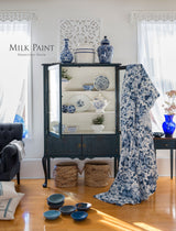 Blue cabinet in Homestead House’s Homestead Blue Milk Paint displaying china, with bowls and floral fabric nearby.