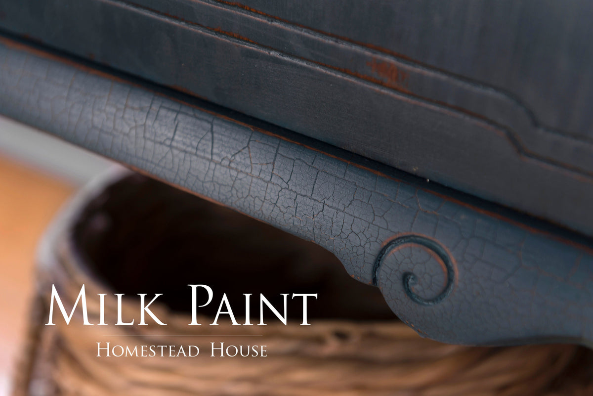 Cracked blue Homestead Blue Milk Paint finish by Homestead House on wood edge, visible branding overlay.