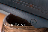 Cracked blue Homestead Blue Milk Paint finish by Homestead House on wood edge, visible branding overlay.