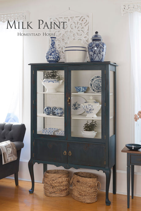 Homestead Blue Milk Paint china cabinet by Homestead House with displayed ceramics and baskets beneath on wood floor.