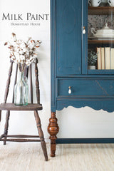 Wooden chair beside blue cabinet in Homestead Blue Milk Paint by Homestead House, with cotton stems on light rug.