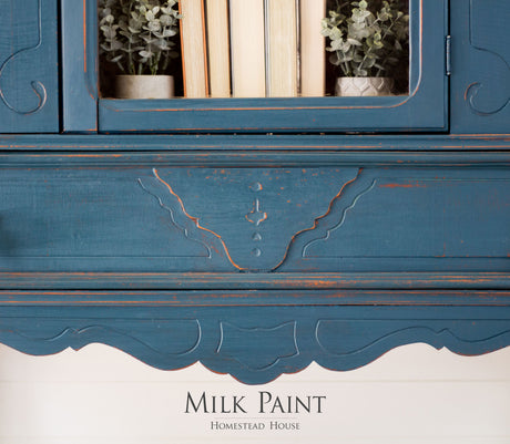Blue cabinet with ornate trim, books, and plants, painted in Homestead Blue Milk Paint by Homestead House.