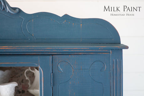 Blue distressed wood cabinet painted with Homestead Blue Milk Paint by Homestead House; brand logo in corner.