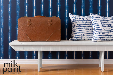 Brown suitcase on a bench painted in Hotel Robe Milk Paint by Fusion, with blue pillows nearby.