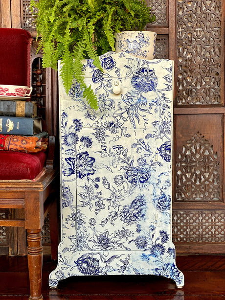 Cabinet with I.O.D. Indigo Floral Paint Inlay beside red chair, topped with a fern and stacked books.