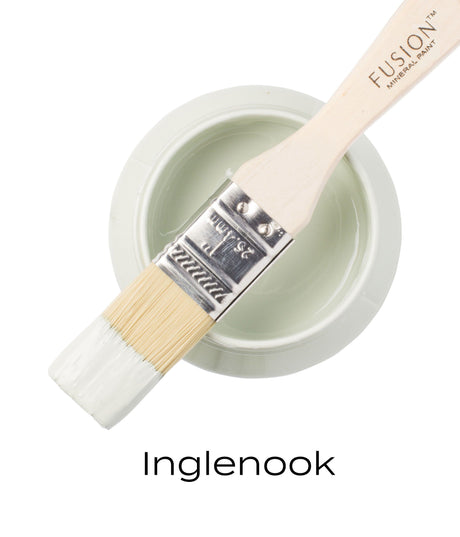 Paintbrush with pale green Inglenook Fusion Mineral Paint resting on a jar labeled Inglenook in black text.