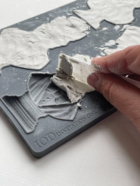 Hand peeling dried clay from I.O.D. Invitation Only Mould, revealing raised patterns and IOD branding.