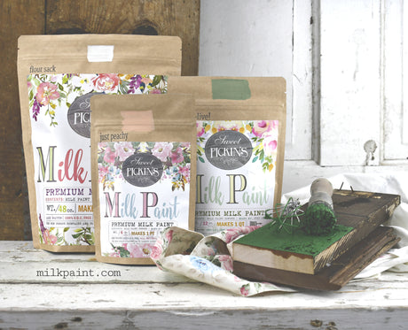 Three Julep Sweet Pickins Milk Paint packs with paintbrush, fabric, and notebook on a white surface.