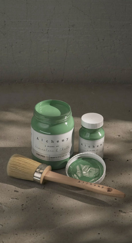 Open jar and closed bottle of Juniper Alchemy Paint by Fusion Mineral Paint with brush and lid nearby on gray surface.
