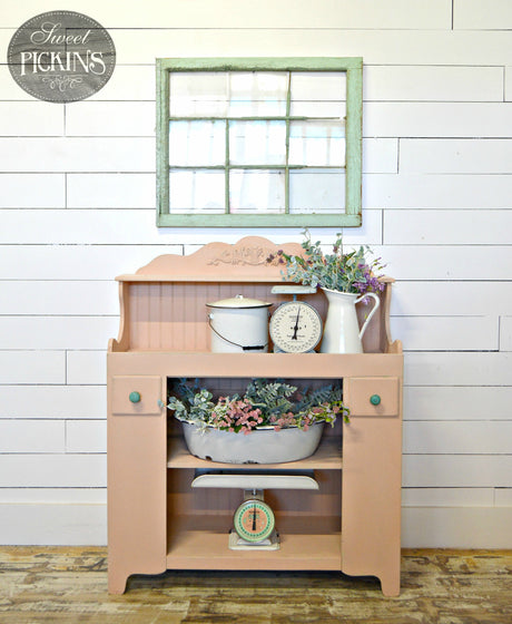 Pink cabinet painted in Old Fashioned Milk Paint’s Just Peachy, with vintage kitchenware and flowers on top.