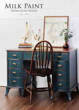 Blue vintage desk with brass handles, brown chair, art supplies, and Homestead House Kentucky Green Milk Paint accents.