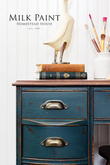 Blue desk painted with Kentucky Green Milk Paint by Homestead House, with books, bird sculpture, and paintbrush jar.