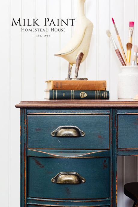 Blue desk painted with Kentucky Green Milk Paint by Homestead House, with books, bird sculpture, and paintbrush jar.