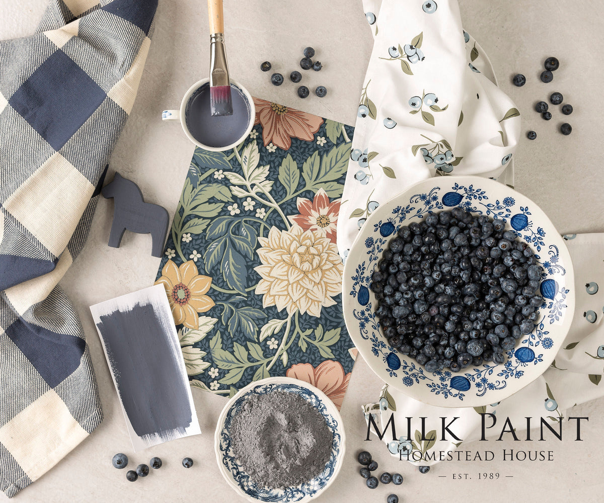 Homestead House Kurbits Indigo Milk Paint with paint supplies and a bowl of blueberries on floral fabric.
