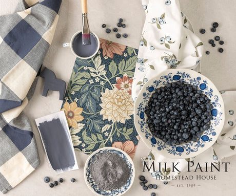 Homestead House Kurbits Indigo Milk Paint with paint supplies and a bowl of blueberries on floral fabric.