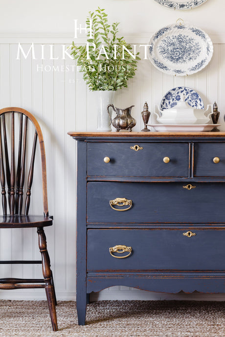 Dresser finished in Homestead House Kurbits Indigo Milk Paint beside a chair, with plates hanging above.