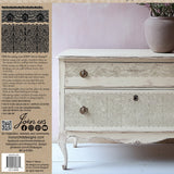 White distressed dresser decorated with I.O.D. Lace Stamp by Iron Orchid Designs, stone vase on left side.