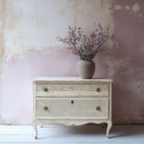 Vintage two-drawer dresser featuring I.O.D. Lace Stamp design, topped with a vase of purple flowers.