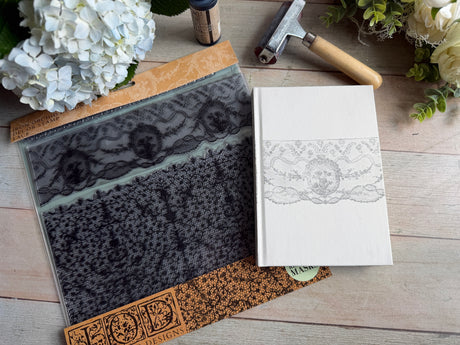 The Lace Stamp by IOD on a white book cover, with flowers and a small hammer nearby.