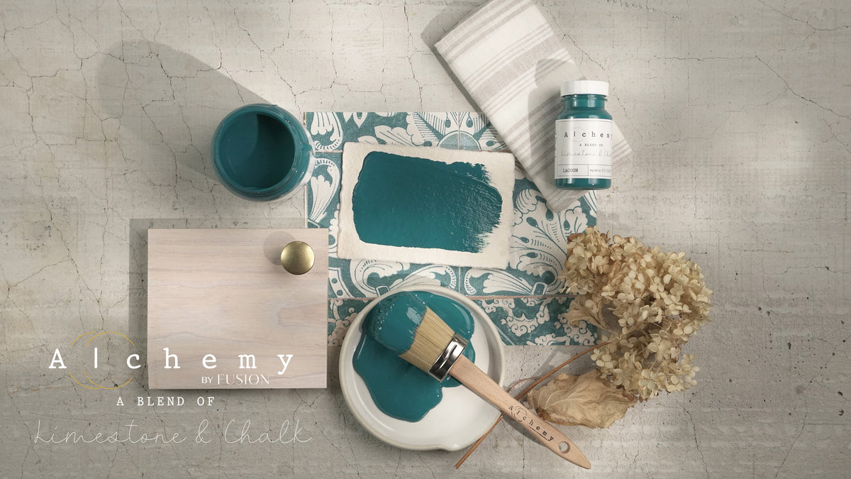Open jar of Lagoon Alchemy Paint by Fusion Mineral Paint with paintbrush, sample cards, and flowers nearby.