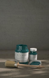 Two jars of Fusion Mineral Paint Lagoon Alchemy Paint with a paintbrush on a gray surface.