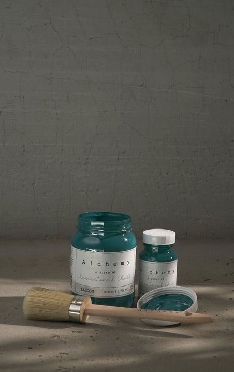 Two jars of Fusion Mineral Paint Lagoon Alchemy Paint with a paintbrush on a gray surface.