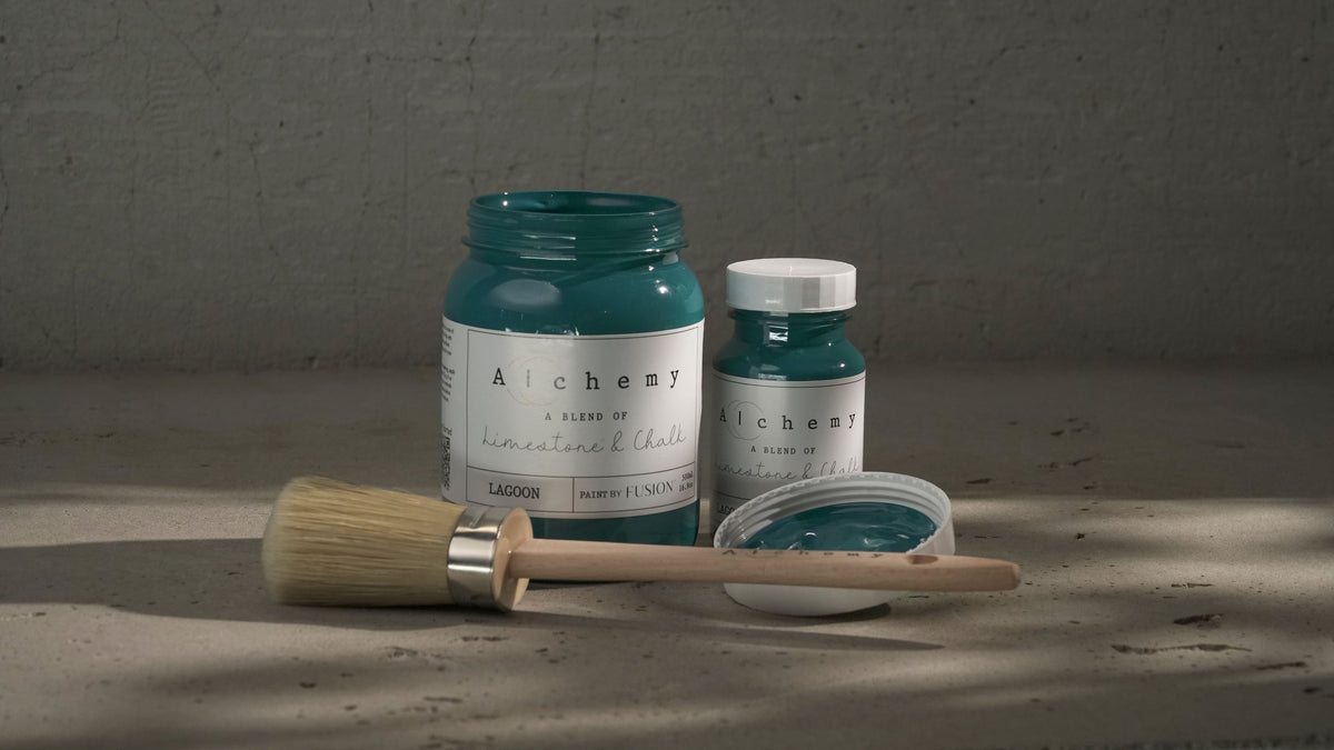 Two jars of Lagoon Alchemy Paint by Fusion Mineral Paint with a brush and painted lid on a gray surface.