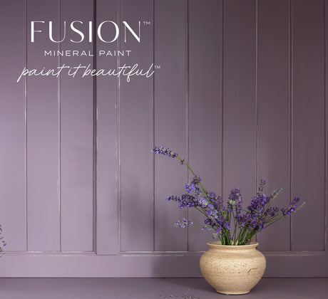 Beige vase with purple flowers in front of a mauve wall painted in Fusion Mineral Paint’s Lavender Haze.