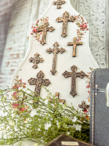 Six ornate I.O.D. Les Croix crosses on a white floral board with decorative blooms and greenery.