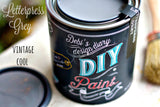 Open can of DIY Paint Co. Letterpress Grey with paintbrush and lid; eco-friendly clay and chalk paint.