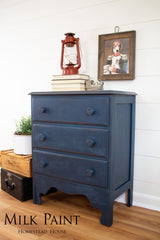 Dresser in Homestead House Liberty Blue Milk Paint with books, red lantern, and framed dog art on top.