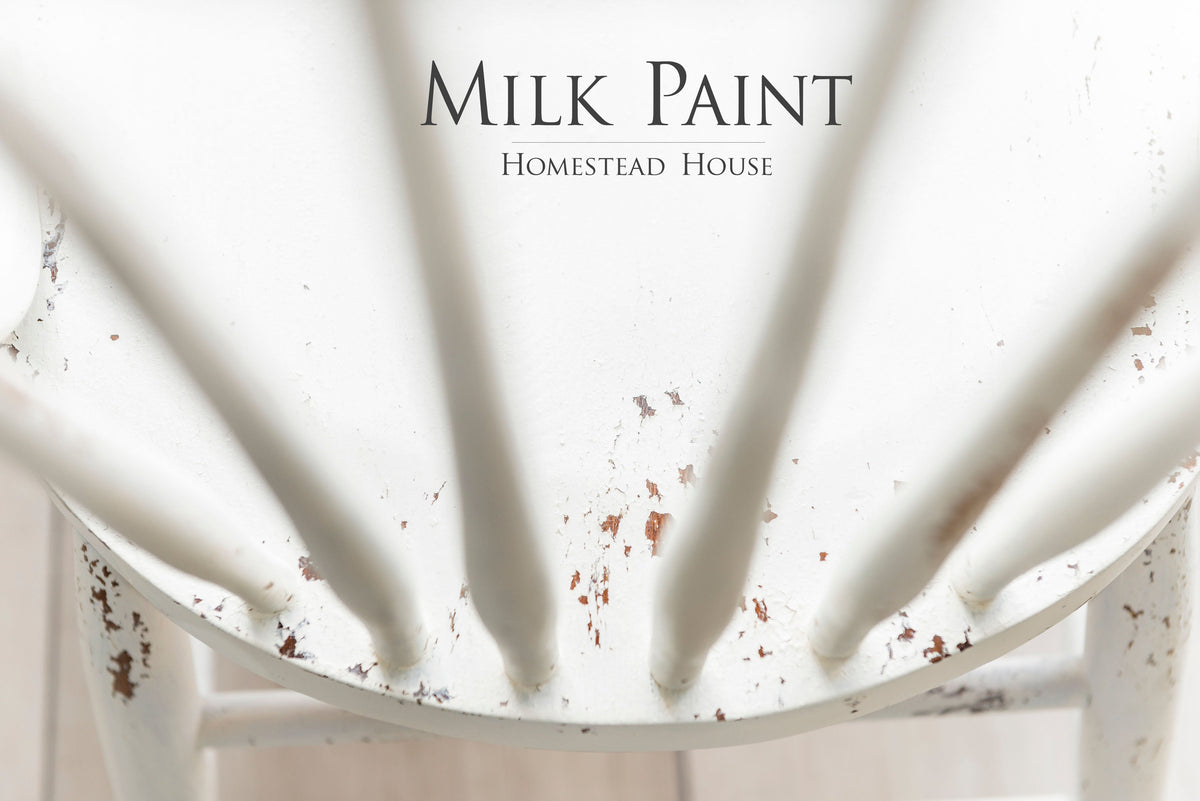 Chipped white wooden chair, Homestead House brand, with “Limestone Milk Paint by Homestead House” text visible.