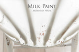 Chipped white wooden chair, Homestead House brand, with “Limestone Milk Paint by Homestead House” text visible.