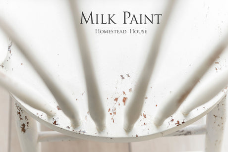 Chipped white wooden chair, Homestead House brand, with “Limestone Milk Paint by Homestead House” text visible.