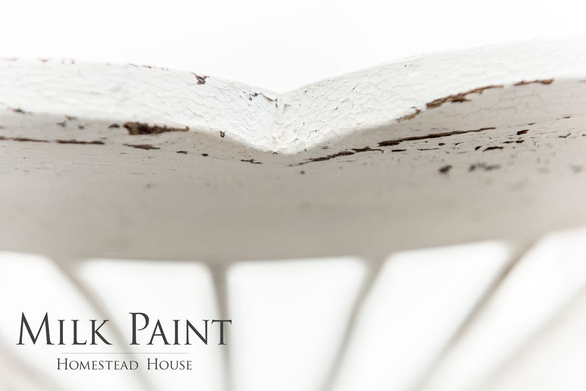 Distressed white chair painted in Limestone Milk Paint by Homestead House, brand text visible in corner.