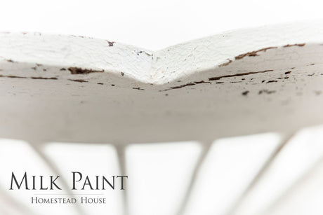 Distressed white chair painted in Limestone Milk Paint by Homestead House, brand text visible in corner.
